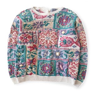 Peut inclure: Un pull patchwork vintage aux couleurs variées, notamment le turquoise, le rose, le violet et le crème. Le pull présente une encolure ras du cou et un motif en tricot texturé. Le motif du pull est composé de carrés et de rectangles.