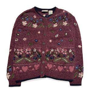 May include: A burgundy cardigan with a floral and heart pattern. The button-up sweater features two pockets and navy trim. The floral design includes pink, blue, and green accents. The sweater is made of a soft, textured material. A vintage style garment.