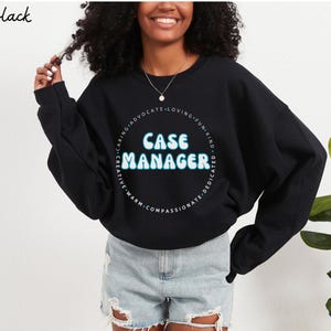 Könnte beinhalten: Schwarzes Sweatshirt mit dem Schriftzug "CASE MANAGER" in hellblauer, umrandeter Schrift. Der Text ist von einem Kreis aus Wörtern wie "kreativ", "fürsorglich" und "mitfühlend" umgeben. Das Wort "Black" steht oben links.