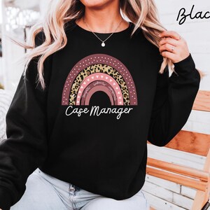 Puede incluir: Sudadera negra con un diseño de arcoíris colorido con detalles de estampado de leopardo. El arcoíris incluye las palabras "Thoughtful, Empathetic, Supportive" y el texto "Case Manager" en escritura blanca. Una prenda superior informal y cómoda.