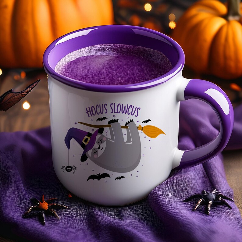 May include: White ceramic mug with a purple interior and handle, featuring a Halloween-themed design. The mug has a cartoon sloth wearing a witch hat and riding a broom, with the text "Hocus Slowcus". Decorative spiders and bats are also included.
