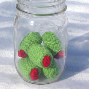 May include: A glass jar filled with crocheted green and red olives. The olives are handmade and have a realistic appearance.