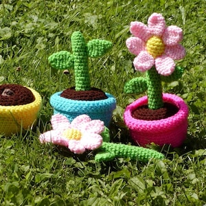 Pode incluir: Quatro vasos de flores de crochê com vasos e flores de diferentes cores. Os vasos são amarelos, azuis, rosa e marrons. As flores são rosa, verdes e amarelas.