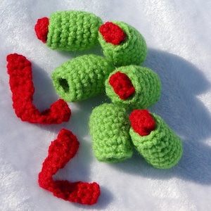 May include: A set of crocheted green and red olive-shaped ornaments. The ornaments are made with a textured stitch and have a red felt detail at the top.