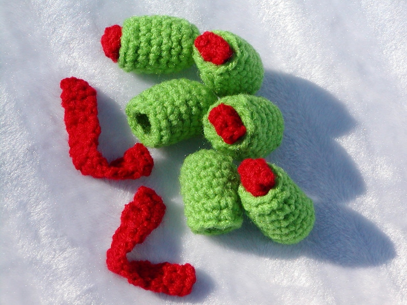 May include: A set of crocheted green and red olive-shaped ornaments. The ornaments are made with a textured stitch and have a red felt detail at the top.