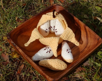 May include: A crocheted pear with a brown stem, open to reveal smaller crocheted pears inside. The pears are in a wooden bowl on a bed of green grass.