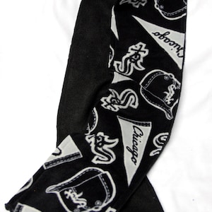 May include: Black and white fleece scarf with a repeating pattern of Chicago White Sox logos, including the team's name, a baseball cap, and a baseball pennant.