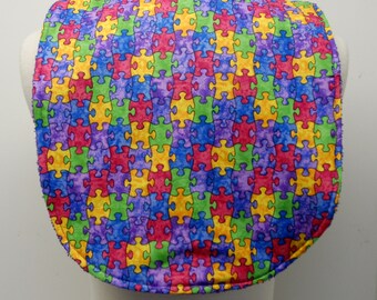 May include: A colorful bib with a puzzle piece pattern in shades of blue, green, yellow, red, and purple.