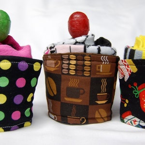May include: Three colorful fabric coffee cup cozies with different patterns. The cozies are made from socks and feature a polka dot pattern, a coffee cup pattern, and a Christmas mitten pattern.