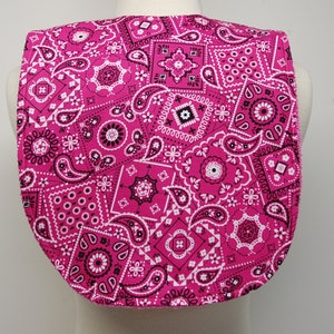 May include: Pink bandana-patterned bib with a rounded neckline. The bib is made of a soft, comfortable fabric and features a black and white paisley design.