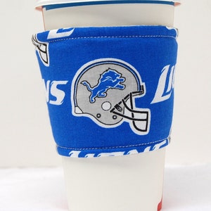 Puede incluir: Un calentador de taza de café de tela azul y blanco con el logotipo de los Detroit Lions y la palabra "Lions" en él.