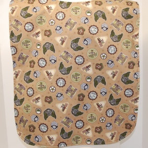 Op de afbeelding: Een beige stoffen slab met een herhalend patroon van militaire patches, waaronder een wereldbol, vleugels en sterren. De patches zijn in tinten bruin, groen en wit.
