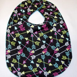 May include: A black baby bib with a colorful arrow pattern. The arrows are in shades of pink, green, blue, and white. The bib has a turquoise trim.