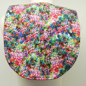 May include: A colorful floral print bib with a rounded neckline and a red trim. The bib is made of a soft, comfortable fabric and features a variety of colors, including red, pink, blue, green, and yellow.