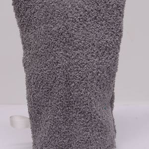 May include: A gray terry cloth mitt with a loop for hanging. The mitt is made of a soft, absorbent material and is designed to be used for washing or exfoliating the skin. The mitt is approximately 8 inches tall.