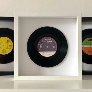 May include: Three framed vinyl records, each with a different album cover. The record on the left has a yellow label with the text "Rollin' Stone" and a red tongue logo. The middle record has a purple label with the text "Pink Floyd - Another Brick in the Wall". The record on the right has a green and orange label with the text "Living on a Prayer".