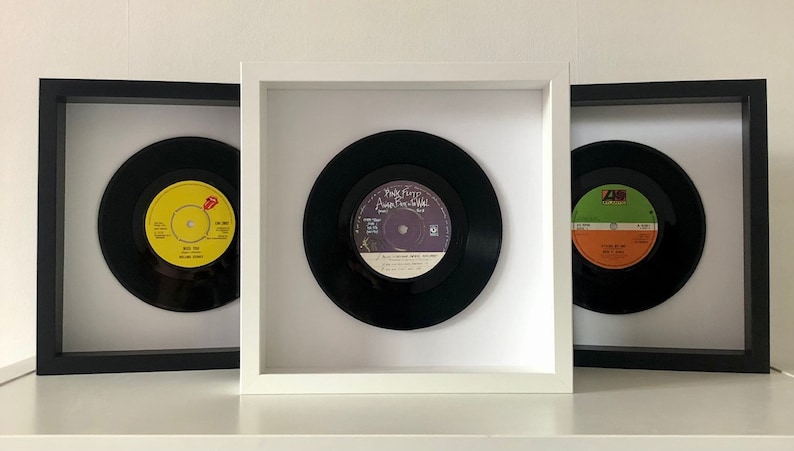 May include: Three framed vinyl records, each with a different album cover. The record on the left has a yellow label with the text "Rollin' Stone" and a red tongue logo. The middle record has a purple label with the text "Pink Floyd - Another Brick in the Wall". The record on the right has a green and orange label with the text "Living on a Prayer".