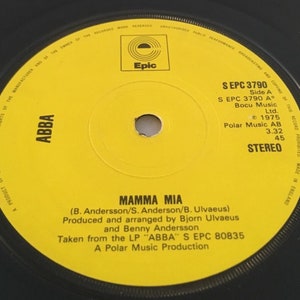 May include: A yellow vinyl record with black text. The record is labeled "ABBA" and features the song "Mamma Mia" by ABBA. The record is from 1975 and is a product of CBS Records.