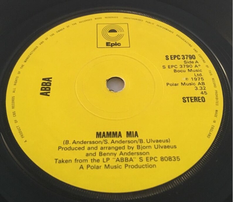 May include: A yellow vinyl record with black text. The record is labeled "ABBA" and features the song "Mamma Mia" by ABBA. The record is from 1975 and is a product of CBS Records.