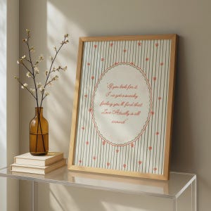 May include: A framed vertical print featuring a cream background with thin vertical green stripes and small red bows. In the center, a scalloped oval frame contains the red text: If you look for it, I've got a sneaky feeling you'll find that Love Actually is all around.
