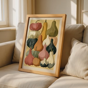 Puede incluir: Una lámina artística enmarcada que presenta una colección de diversas calabazas y calabacines en tonos apagados de rojo, naranja, verde y crema. La ilustración muestra un surtido de formas, incluyendo variedades redondas, en forma de pera y alargadas sobre un fondo amarillo.
