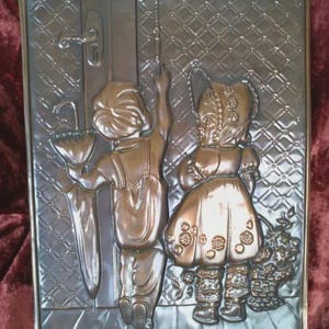May include: A bronze relief sculpture showing two children, one with an umbrella, at a doorway. The artwork has a detailed texture and a decorative border. The children are in vintage clothing, evoking a nostalgic theme. The sculpture is framed.