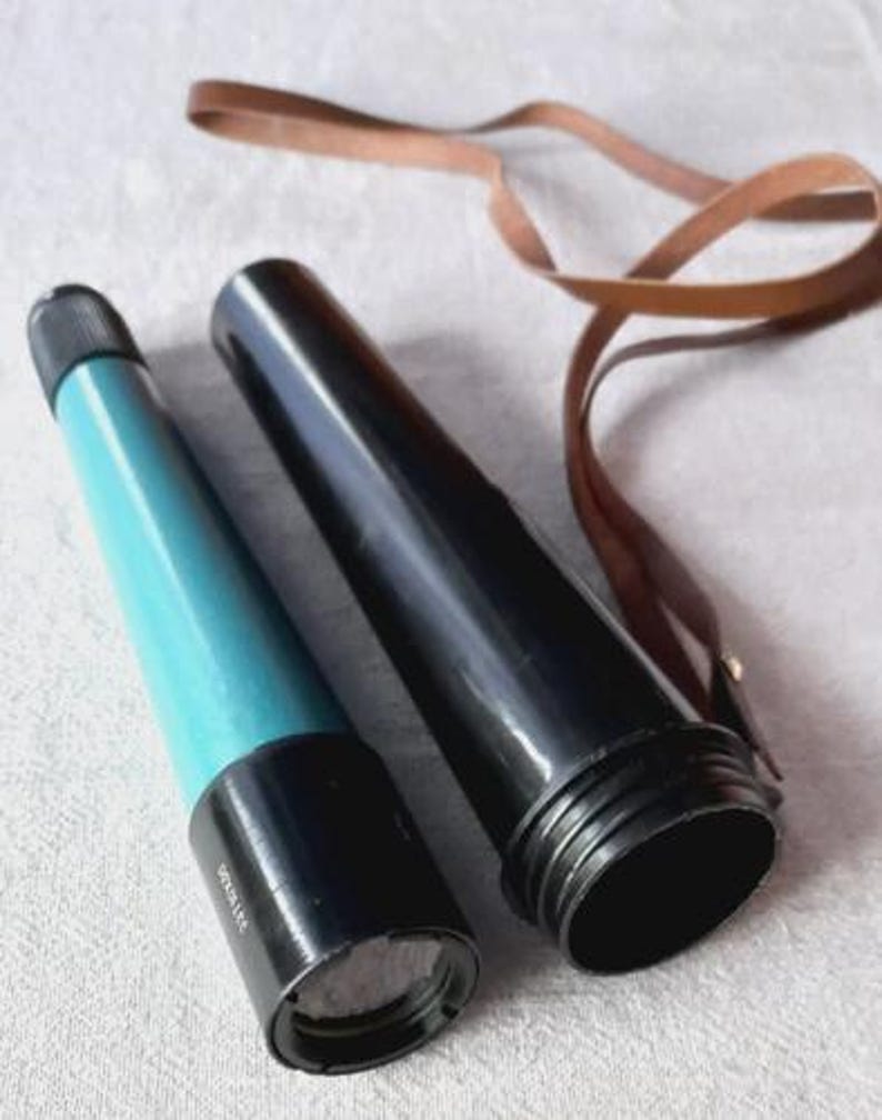 May include: A vintage telescope with a black and teal body, and a brown leather strap. The telescope is in two parts, with one section teal and the other black. The leather strap is coiled next to the telescope.