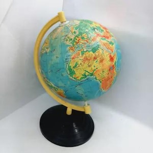 Puede incluir: Un globo terráqueo vintage con base negra y meridiano amarillo. El globo presenta un mapa colorido con océanos azules y continentes en tonos verdes, amarillos y naranjas. Un artículo educativo o decorativo clásico.