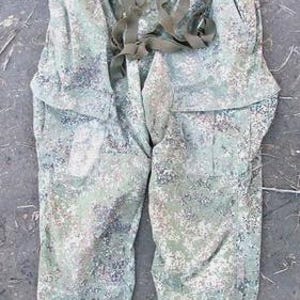 May include: Camouflage pants in shades of green, brown, and gray. The pants have a loose fit, pockets, and adjustable straps. The fabric has a mottled pattern, and the pants appear to be made of a durable material.