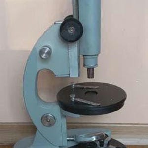 May include: A vintage microscope with a light blue frame and a black circular stage. The microscope has a silver eyepiece and a black base. It is designed for scientific or educational use.