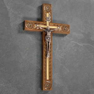 May include: Wooden crucifix with a detailed carving and a bronze-colored figure of Jesus. The cross has decorative floral patterns and a gold-colored accent. A religious item for home decor.