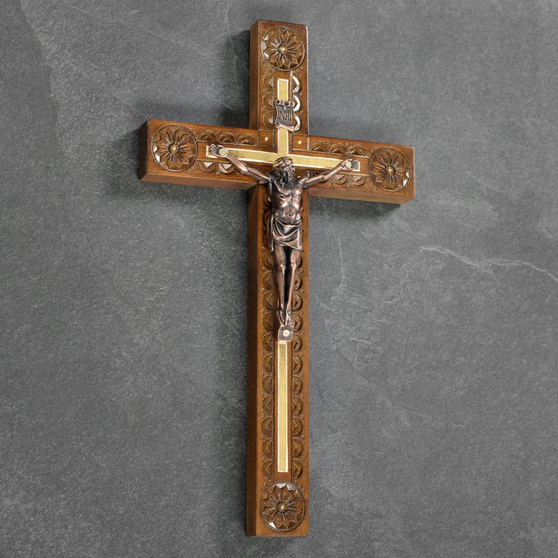 May include: Wooden crucifix with a detailed carving and a bronze-colored figure of Jesus. The cross has decorative floral patterns and a gold-colored accent. A religious item for home decor.