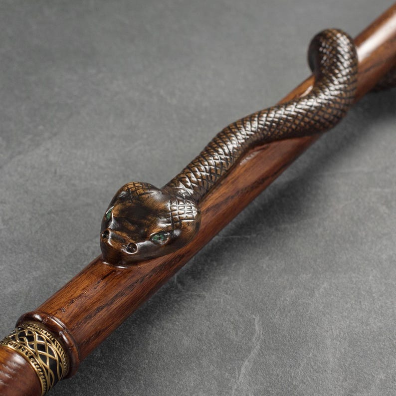 May include: A wooden walking stick with a carved snake head at the top. The snake has green eyes and a brown and black body.