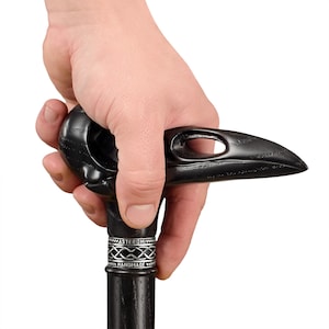 May include: A black walking stick with a carved raven head handle. The handle has a silver band with the words "Asteroma Handmade".
