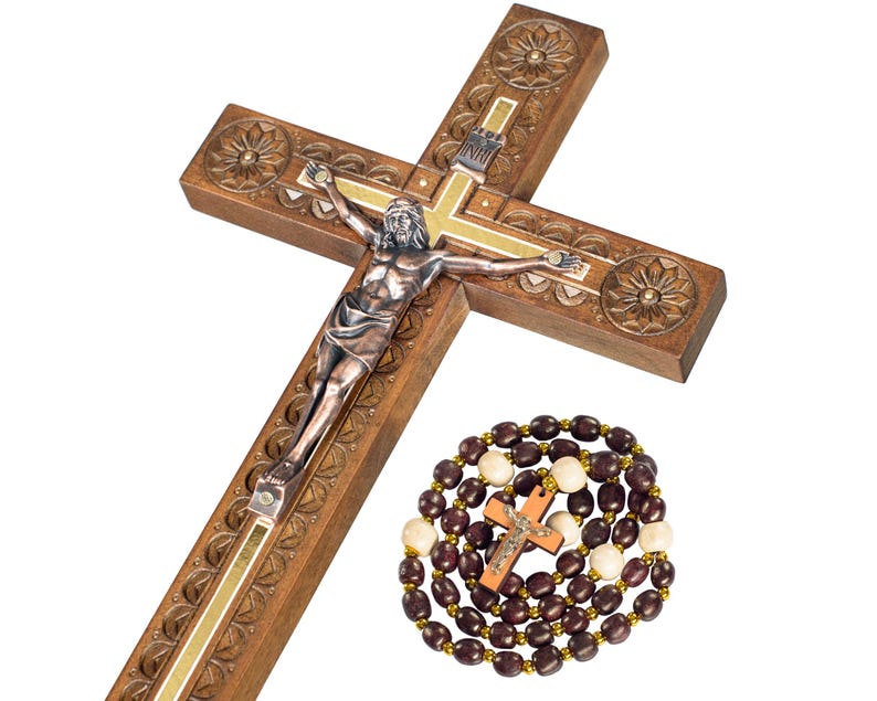May include: A wooden crucifix with a silver-toned Jesus figure and decorative carvings. A rosary with brown and cream-colored beads and a small wooden cross is also present. The cross is approximately 18 inches long.