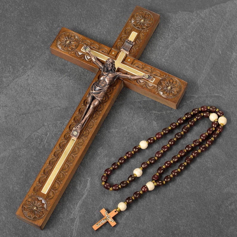 May include: A wooden crucifix with a bronze figure of Jesus Christ and a rosary. The cross is carved with floral designs and has a gold-colored inlay. The rosary features dark brown beads and cream-colored accent beads.
