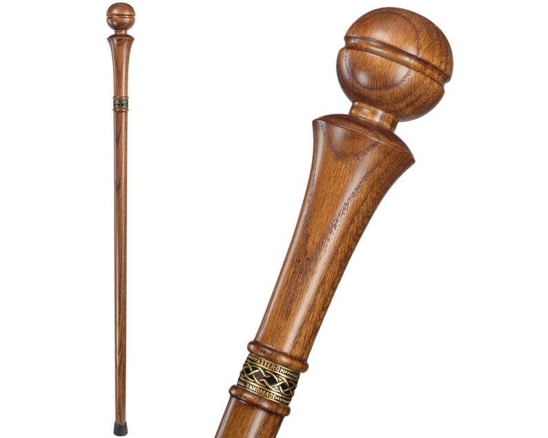 May include: A wooden walking stick with a rounded knob handle and a decorative metal band. The stick is brown and has a natural wood finish.
