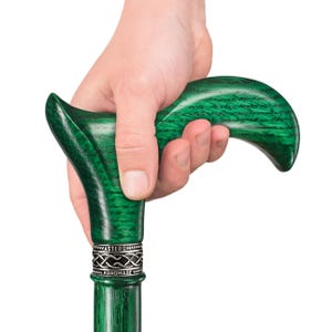 May include: A green wooden walking stick with a carved handle and a silver band with the words "Asterom Handmade".