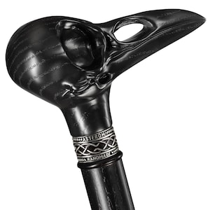 May include: Black wooden walking stick with a carved raven skull handle. The handle has a silver band with the words "Asterom Handmade".