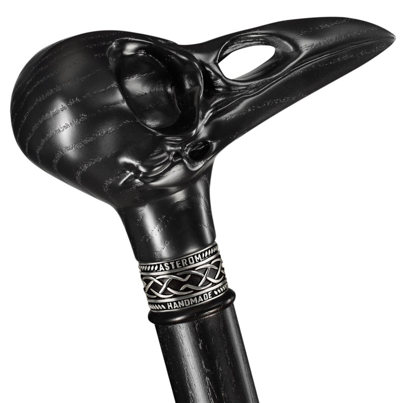 May include: Black wooden walking stick with a carved raven skull handle. The handle has a silver band with the words "Asterom Handmade".