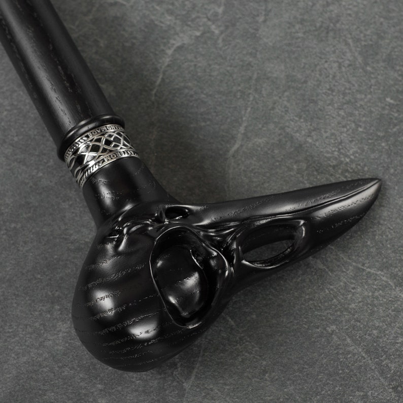 May include: A black walking stick with a detailed carved bird head handle and a silver band.