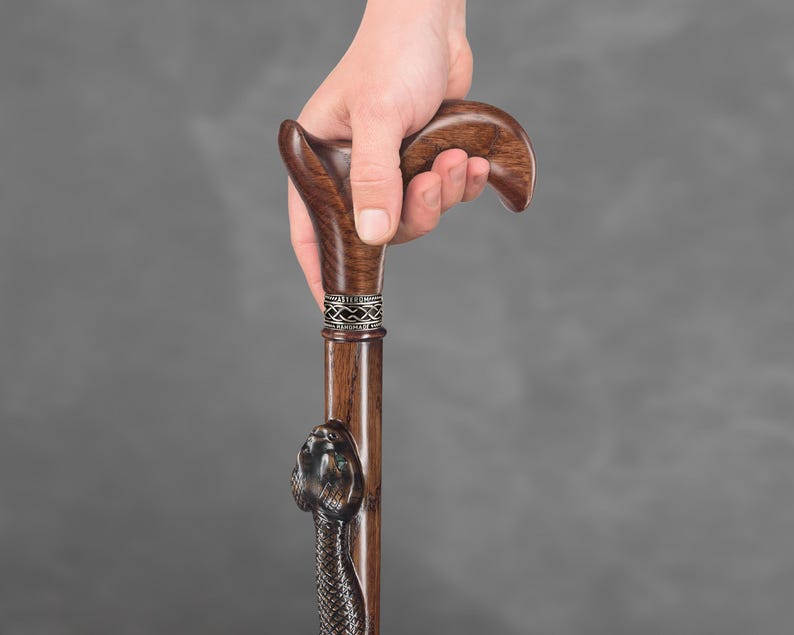 May include: A wooden walking stick with a snake head carved into the bottom of the shaft. The handle is a dark brown colour and has a decorative silver band.
