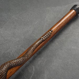 May include: A wooden walking stick with a carved snake design. The stick has a black rubber tip.