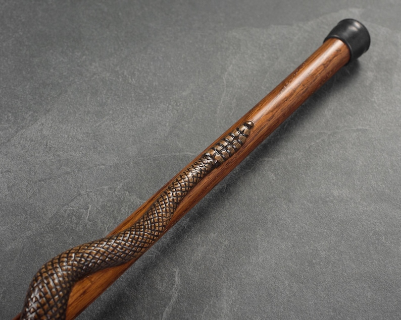 May include: A wooden walking stick with a carved snake design. The stick has a black rubber tip.