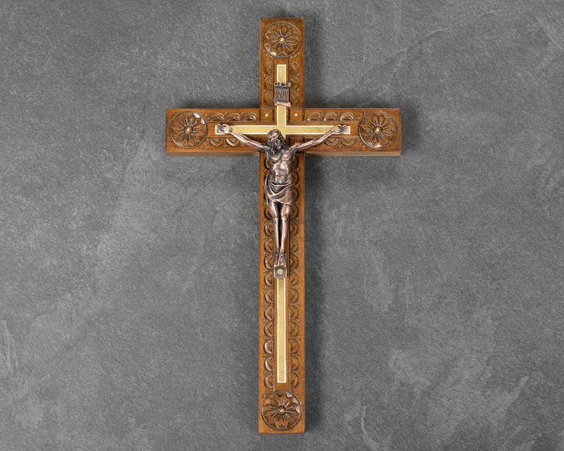 May include: Wooden crucifix with a detailed carved design. The cross features a silver-toned figure of Jesus Christ. The cross is made of brown wood with gold accents and decorative floral carvings.
