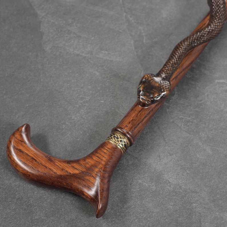 May include: A wooden walking stick with a carved snake head at the top. The stick is brown and has a gold band around it.