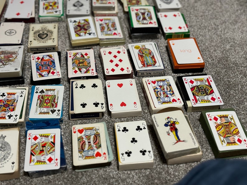 May include: A collection of playing cards in various suits and numbers, including a joker, king, and queen. The cards are arranged in rows on a brown surface.