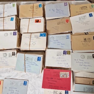 May include: A selection of vintage envelopes in various colours, including white, beige, and red, with stamps and handwritten addresses. Some envelopes are tied with twine. The image showcases a variety of postal ephemera.