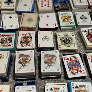 May include: A collection of playing cards in various designs and colors, including a joker card, a queen of hearts, and a card with the text "JOKER" on it.