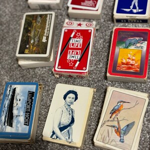 May include: A collection of vintage playing cards featuring various designs. The cards include a red deck with stars and the words "Time Life", a blue deck with a ballerina, a deck with a ship and the words "Northern Prince", a deck with a queen, and a deck with a ship and the words "Import Holt Line Limited".